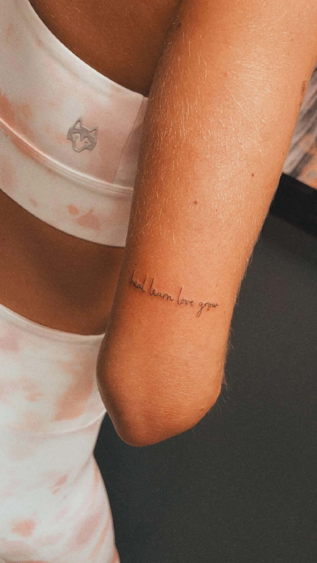Arm with tattoo 'heal learn love grow' and wearing a patterned sports bra.