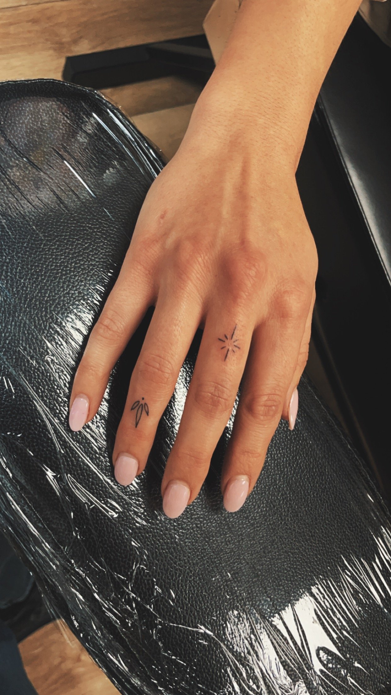 Close-up of a hand with two small finger tattoos on a cushioned surface.