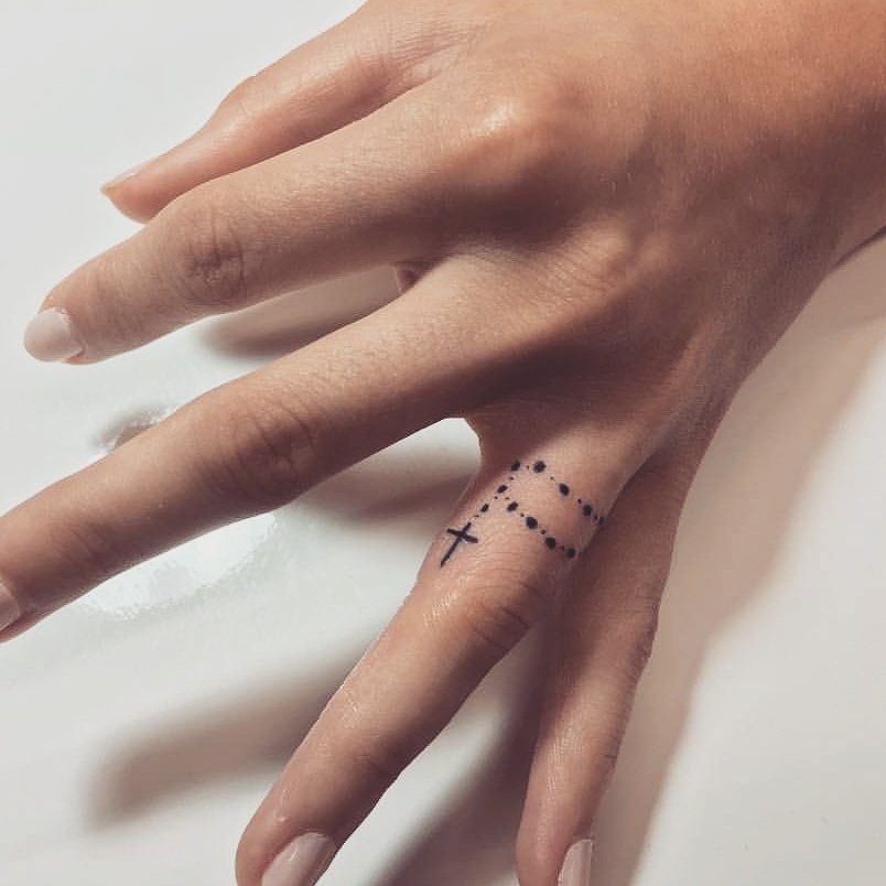 Hand with a small cross and dot tattoos on finger