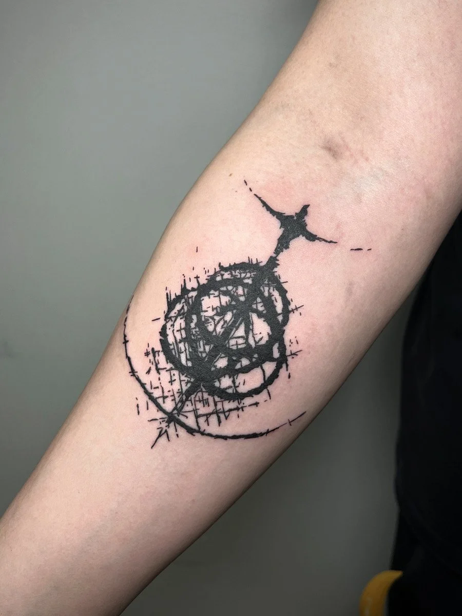 Black ink abstract tattoo on forearm with circular geometric shapes with crosshatch shading.