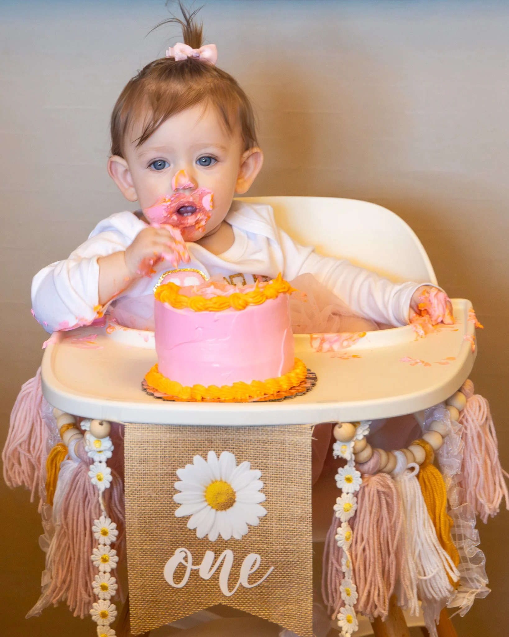 One-year-old girl eating a birthday cake in a high chair, covered in frosting.