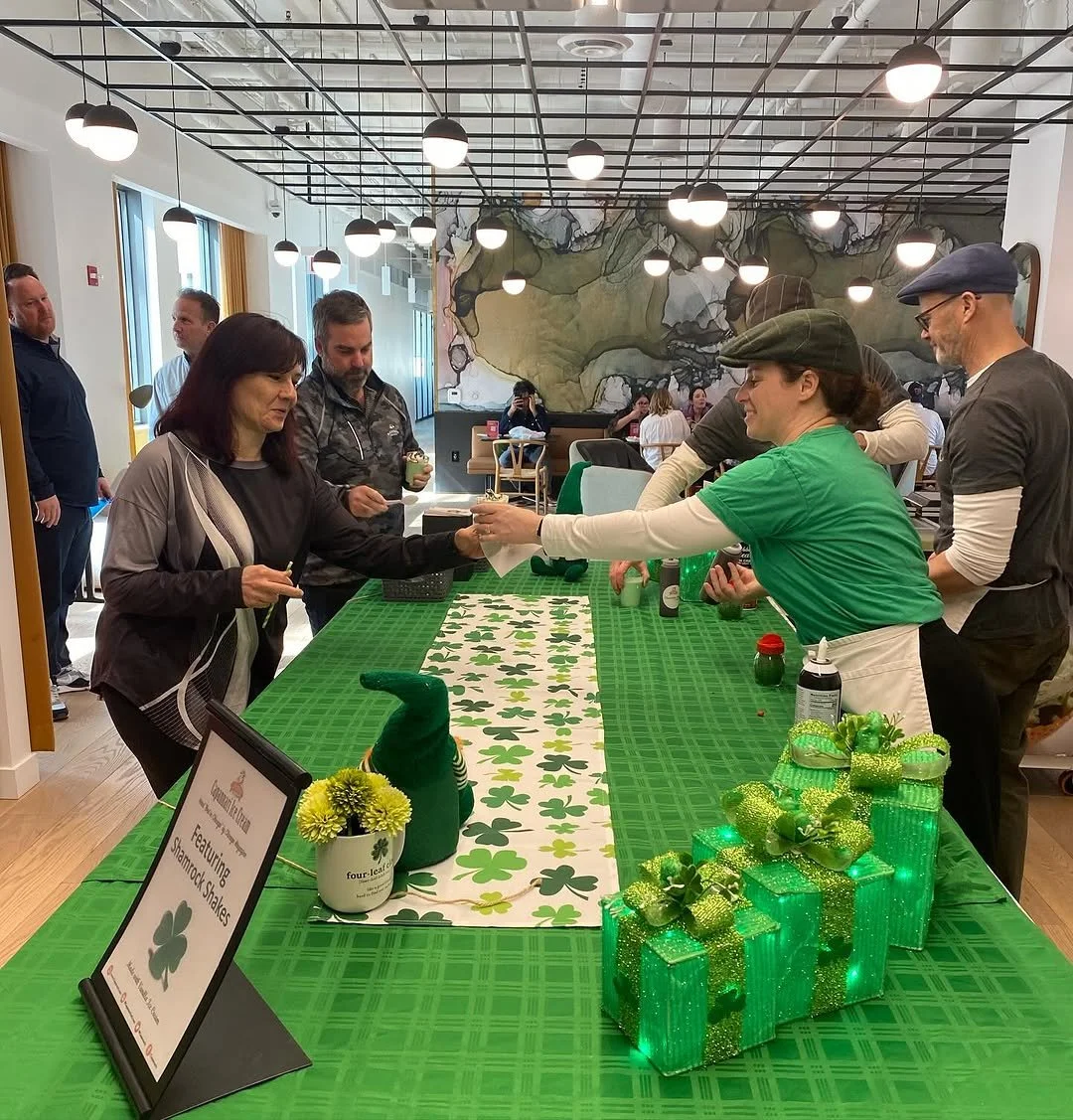 People at a St. Patrick's Day celebration with a green tablecloth, shamrock decorations, and a sign featuring a shamrock on the table.