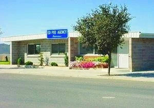 Small commercial building with a sign reading "Ed Poe Agency Insurance" and a landscaped front with plants and flowers.