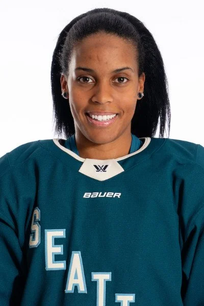 A female athlete in a teal Seattle sports jersey with the word 'SEATTLE' on it, smiling at the camera.