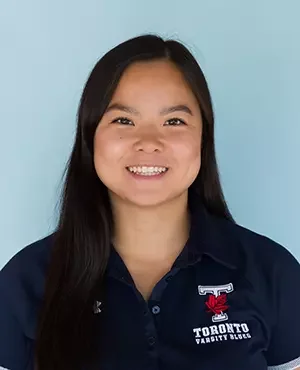 Young woman with long dark hair smiling, wearing a navy blue polo shirt with a Toronto Varsity Blues logo, against a light blue background.