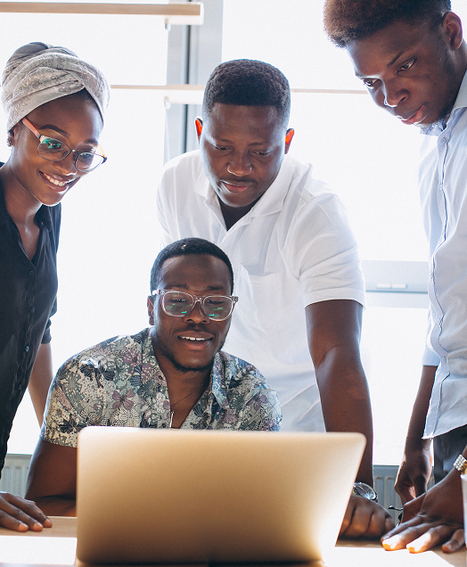 Four young adults gathered around a laptop, looking at the screen in a bright office.