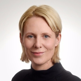 Close-up portrait of a woman with short blonde hair, wearing a black top, smiling slightly.