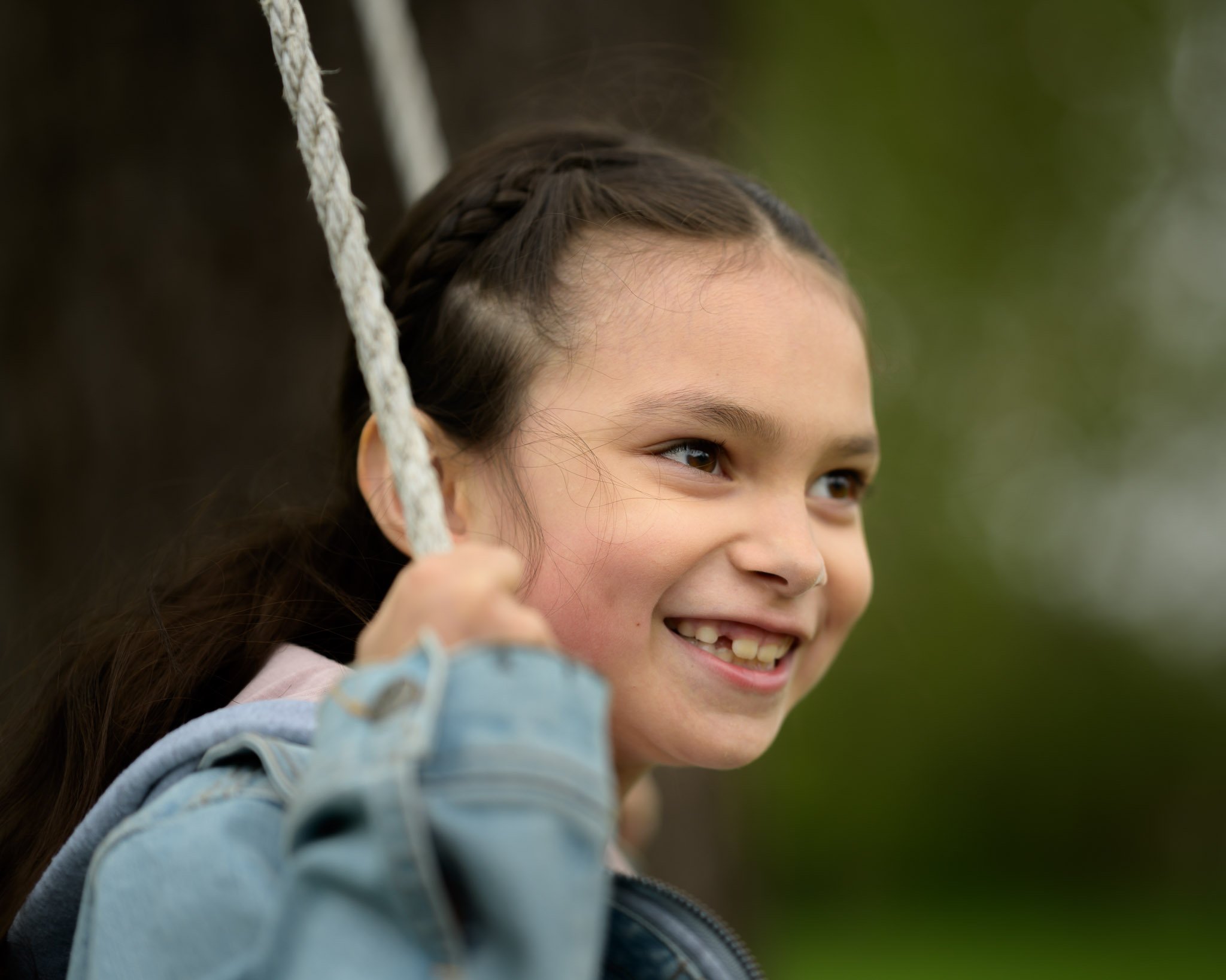 A young girl smiling while holding onto a rope swing outdoors. Family photography at local park Eugene Oregon.
