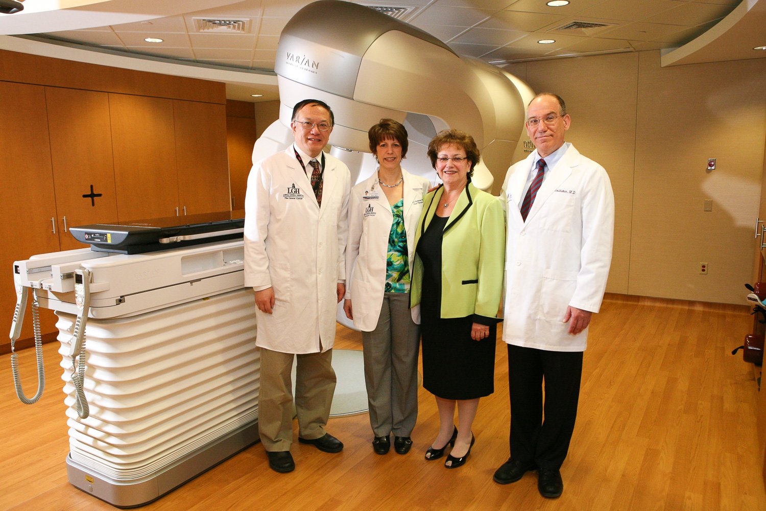 Four people standing in a medical facility, two wearing white lab coats, posing near a Varian radiation therapy machine.