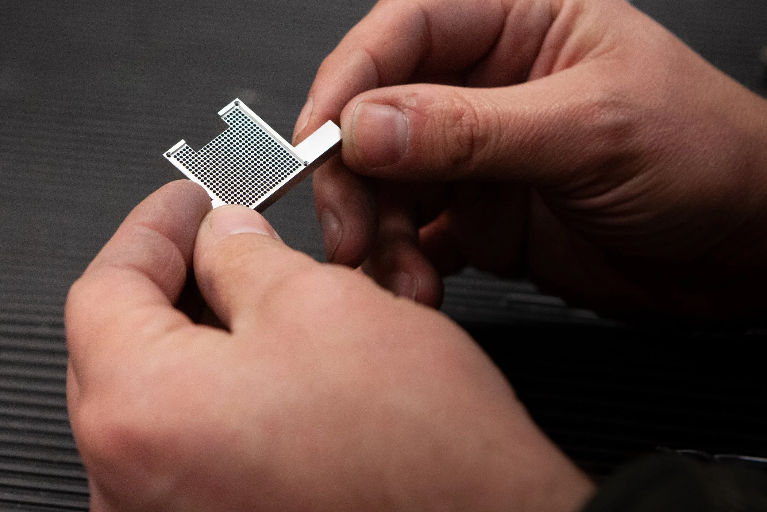 Hands holding a small metal component with a grid pattern