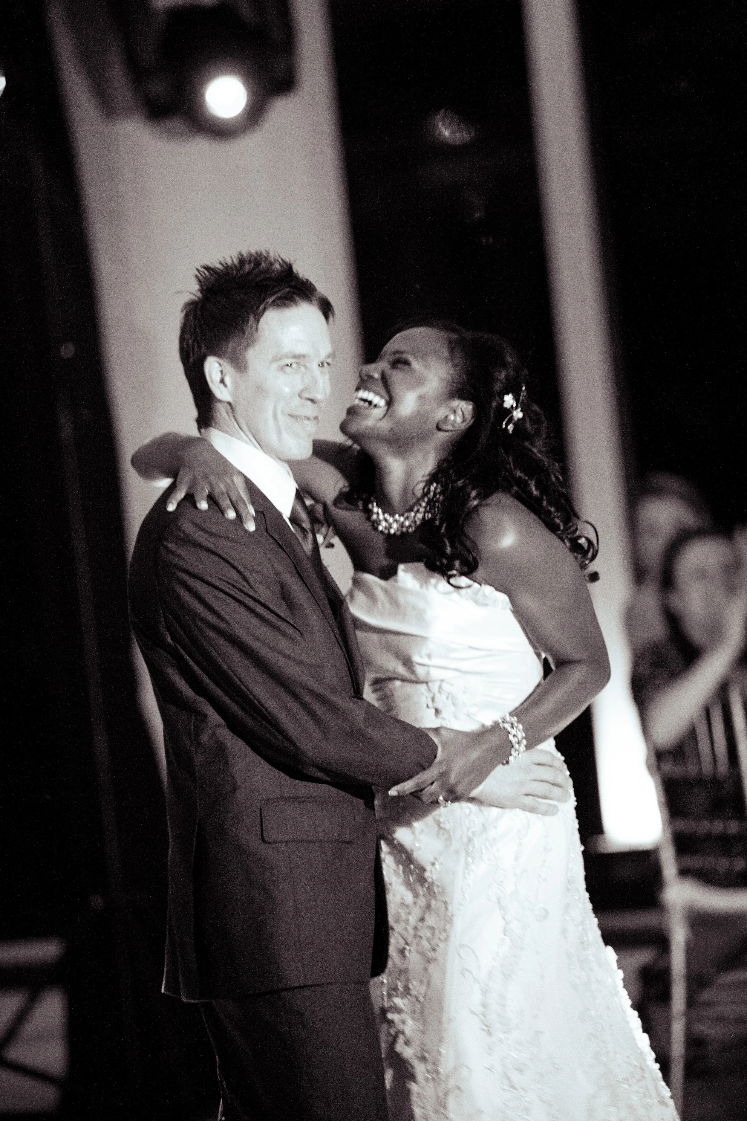A black-and-white photo of a joyful couple dancing at their wedding, a bride and groom smiling and holding each other.