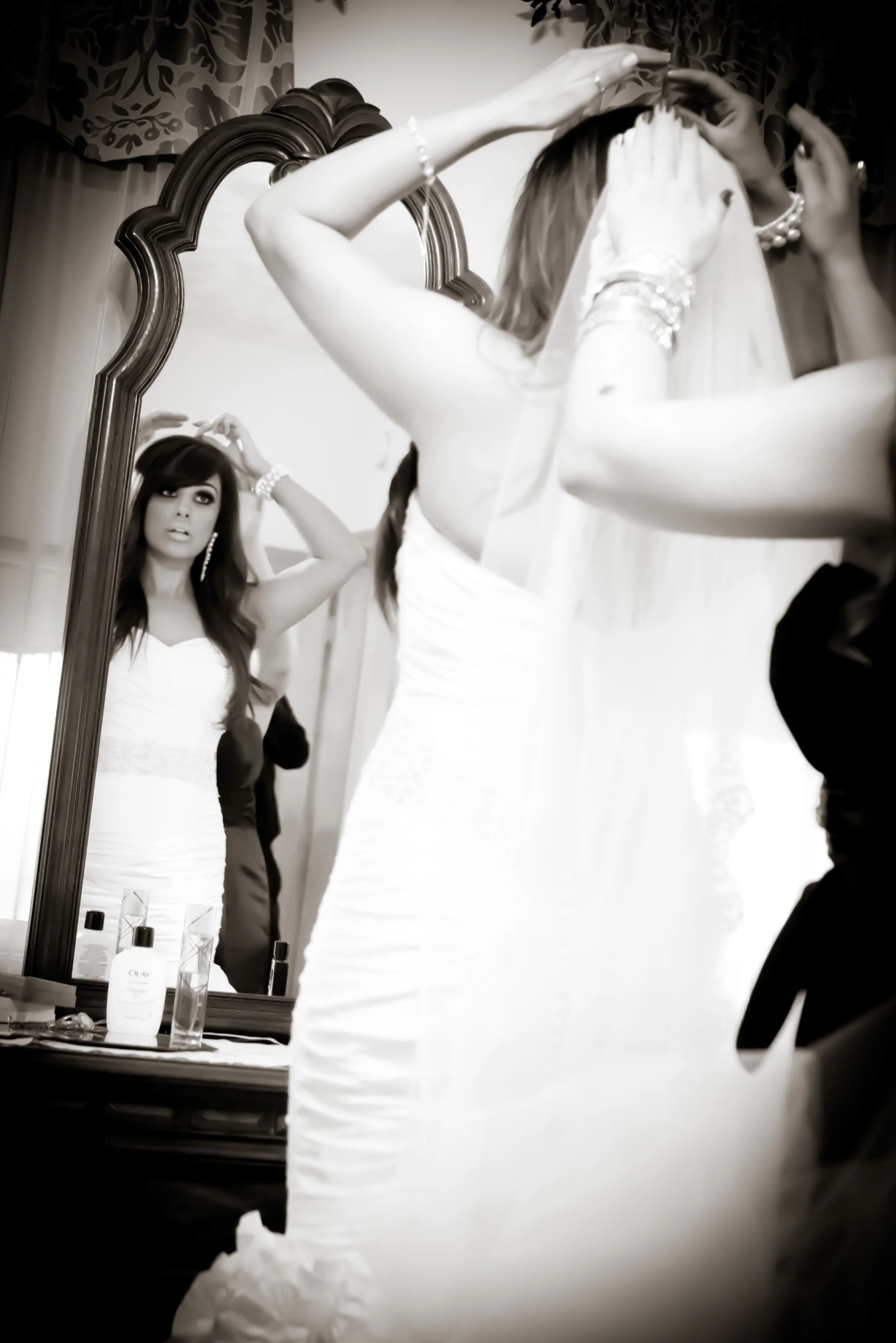 A bride in a wedding dress is looking at herself in a mirror while adjusting her hair. She is getting ready before the wedding.