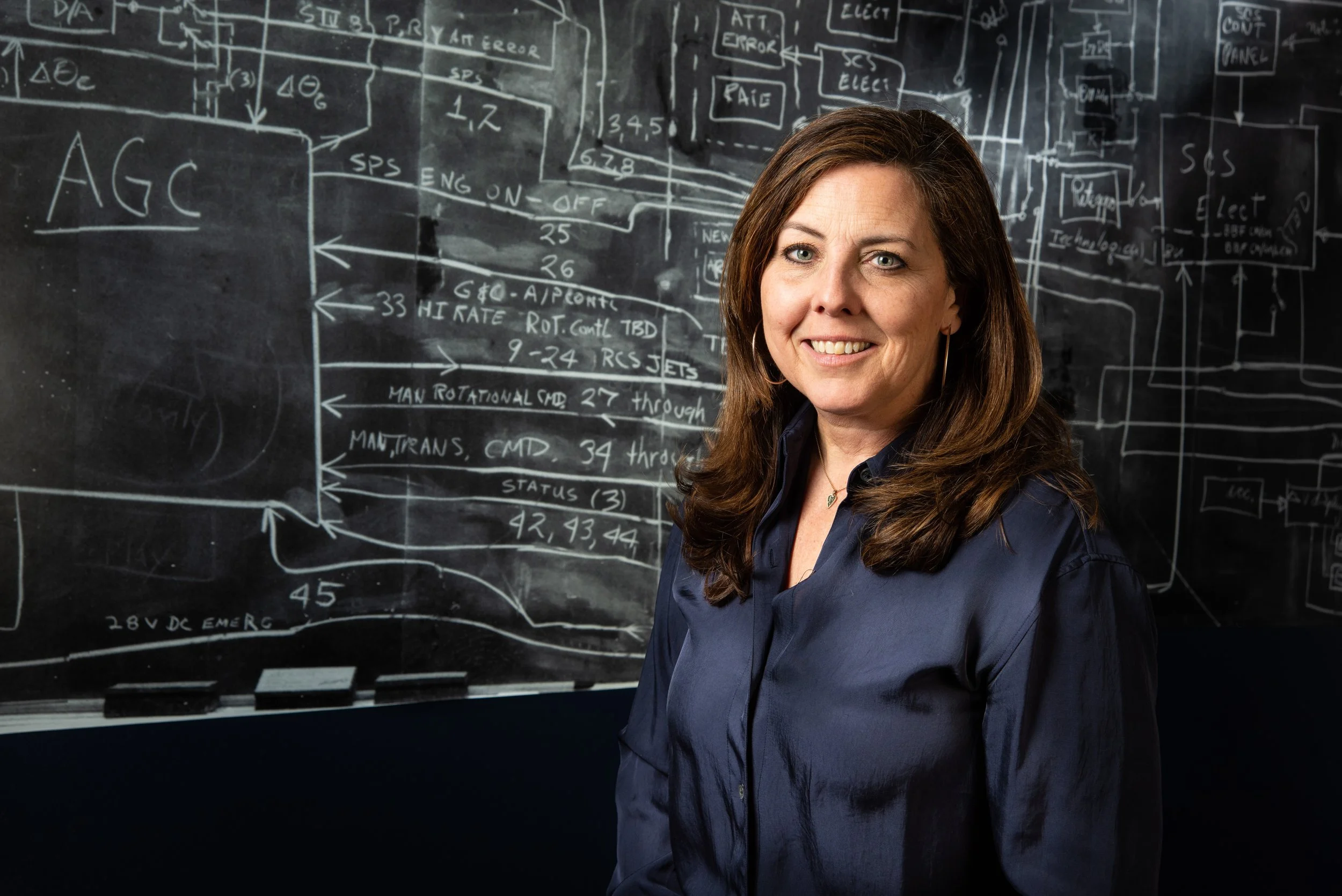 Woman standing in front of a chalkboard with technical diagrams and text.