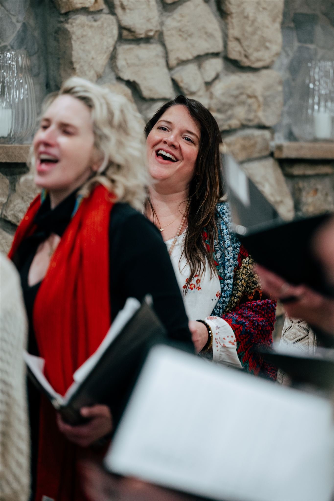 Group of people smiling and singing inside a stone-walled room, with some holding songbooks.