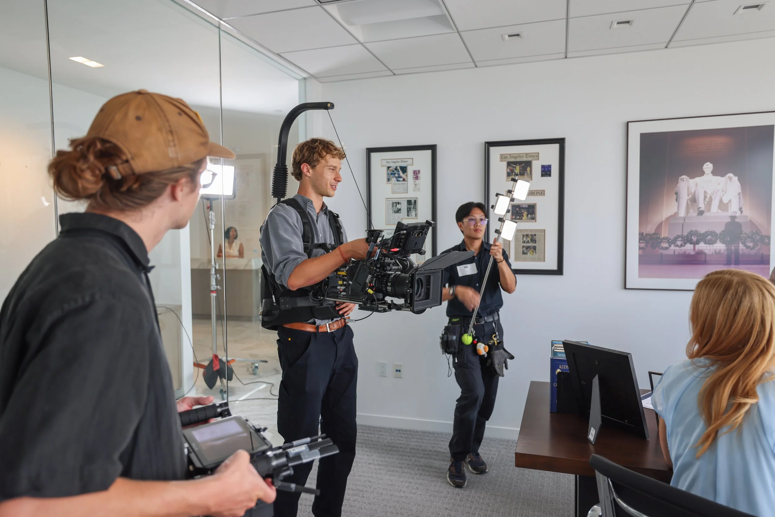Filming crew setting up equipment for a video interview inside an office, with framed photos and a large photograph of the Lincoln Memorial in the background.