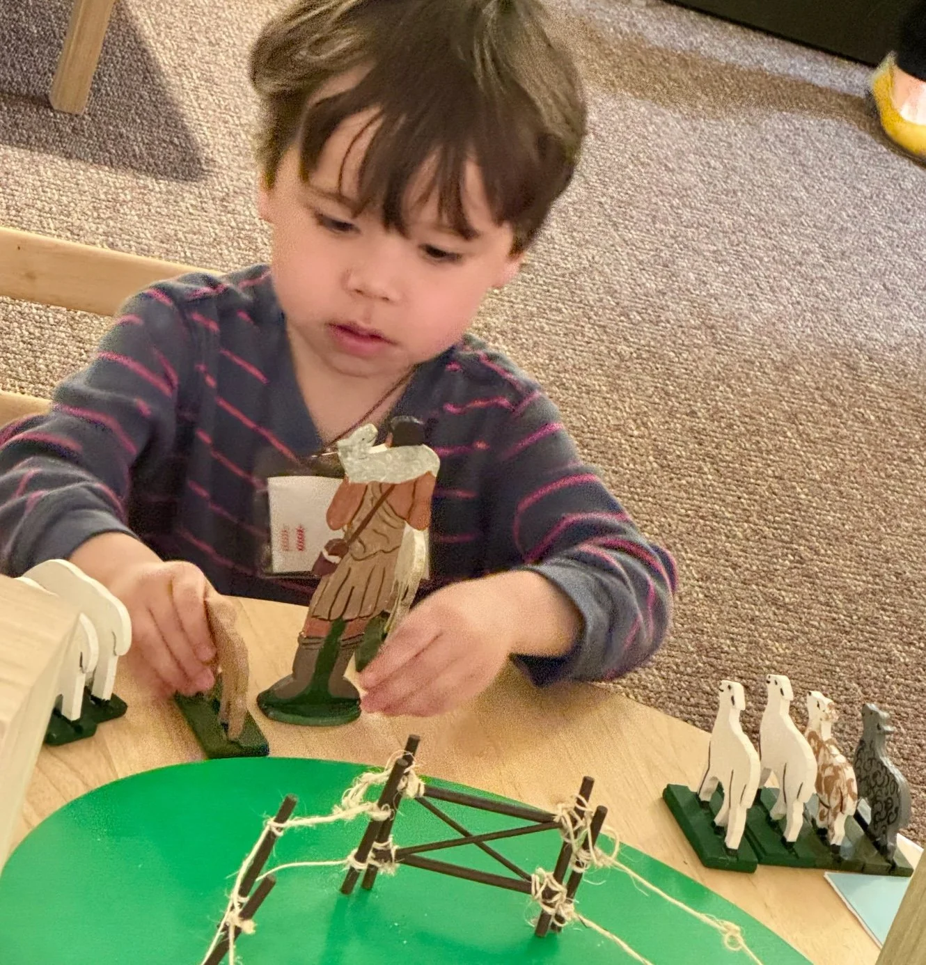 A young child playing with wooden animal figurines and a small bridge model on a table.