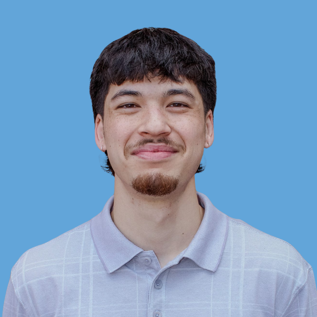A young man with dark hair and a mustache smiling against a blue background.