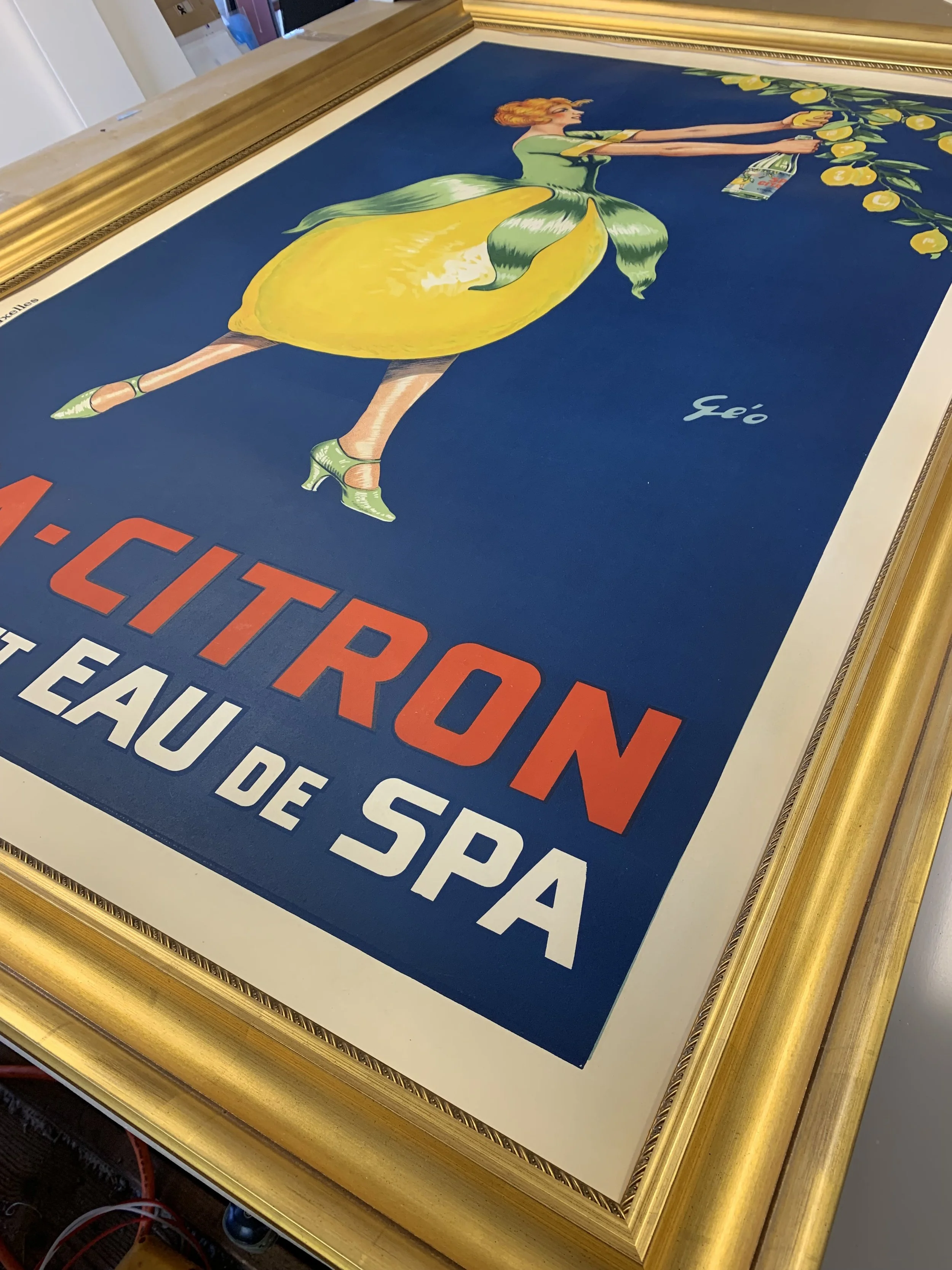 An original French poster from the 1920s featuring a whimsical woman dressed as a lemon in a chunky, ornate gold archival frame. 