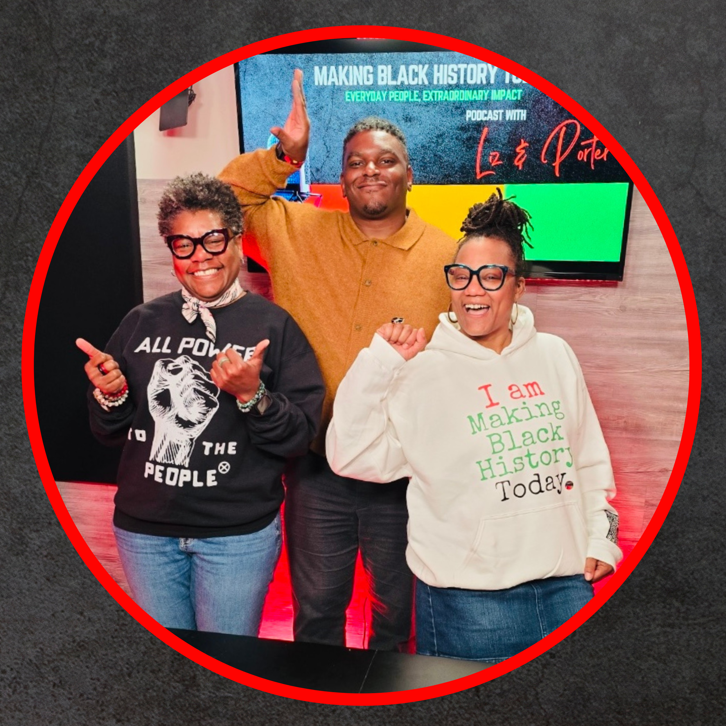 Three people smiling and posing in front of a TV screen at a podcast event. The person on the left is wearing a black sweatshirt with a graphic and text. The person in the middle is wearing a brown shirt, and the person on the right is wearing a white hoodie with text. They are making celebratory gestures.