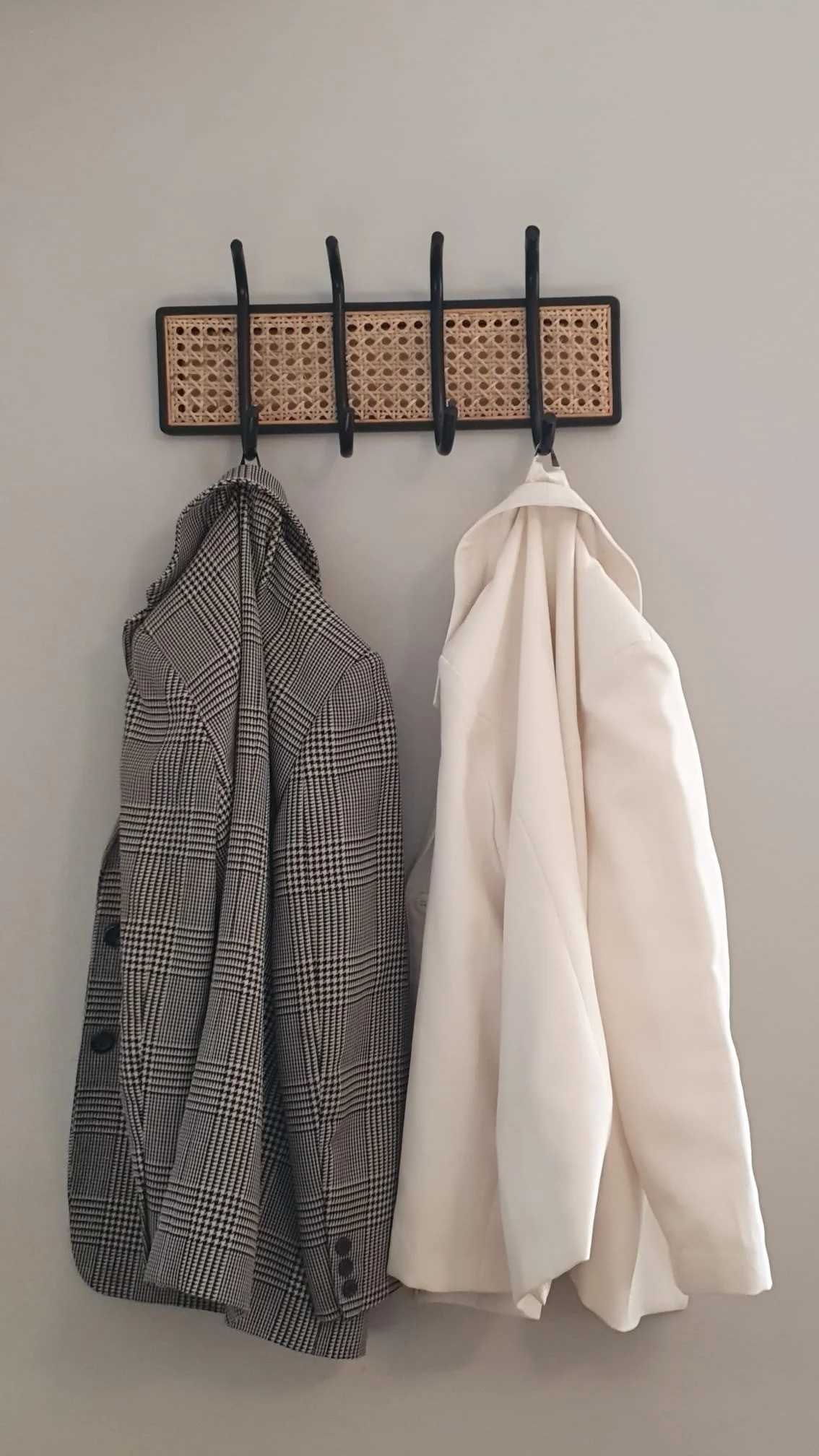 Wall-mounted coat rack with five black hooks, holding a houndstooth patterned blazer and a white hoodie.