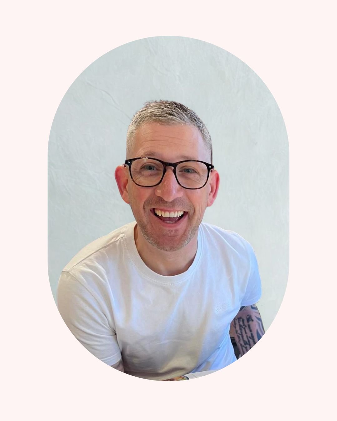 A smiling man with short gray hair, glasses, and a white t-shirt, looking directly at the camera, against a light-colored background. Life Coach Lama client success - Life Coach London - Lama Abou Daher