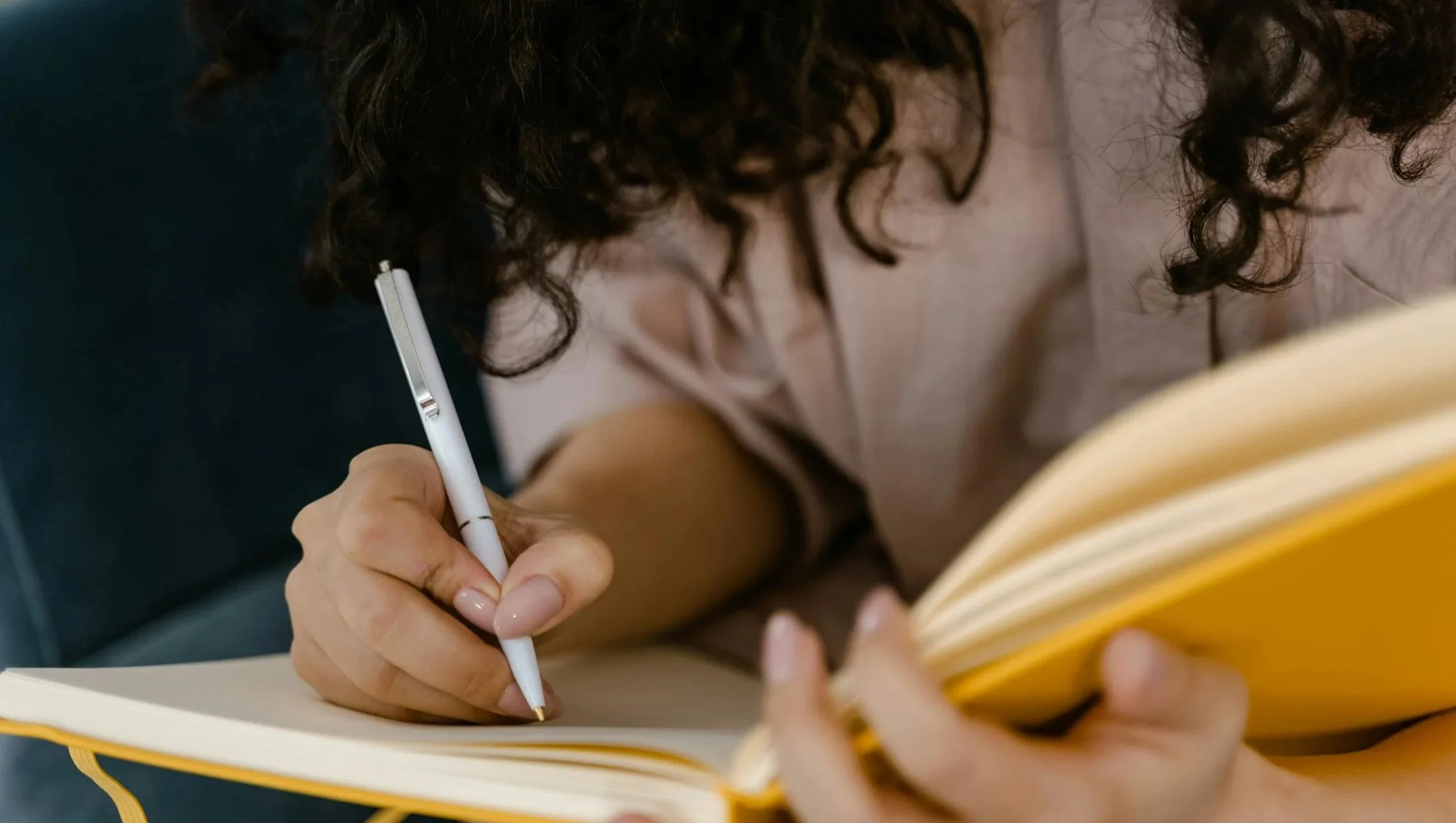 Woman writing by hand in a yellow notebook.
