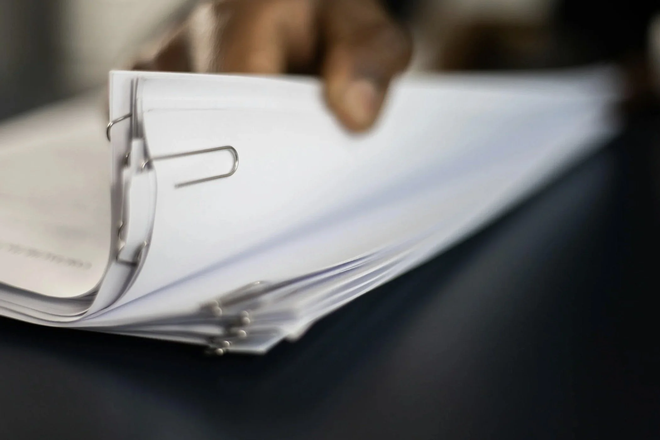 Fingers holding a stack of papers, held together with a paperclip