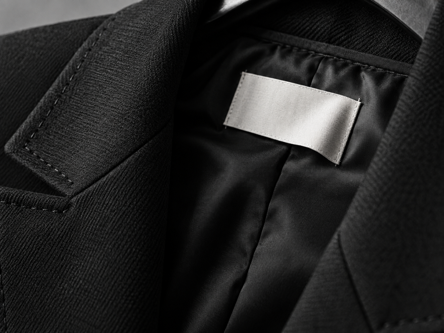 Close-up of black tailoring, fine stitching, and a blank ivory garment label.