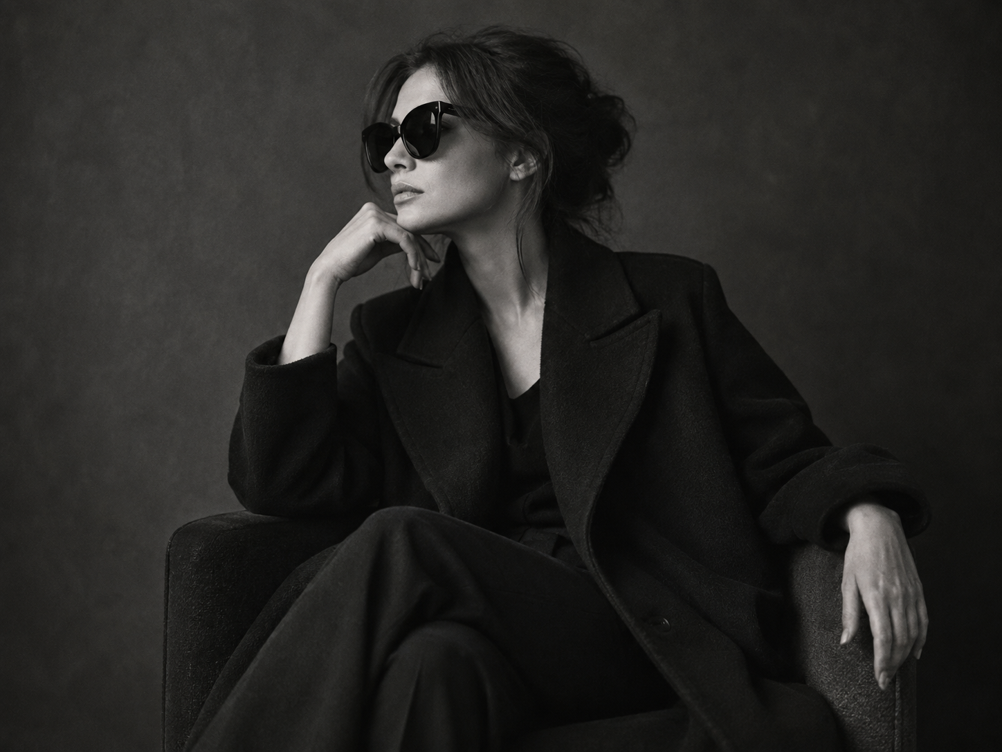 Black-and-white portrait of a woman in a tailored black coat and sunglasses.