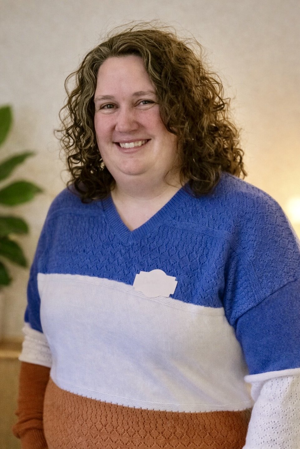 Cheryl Davis, she has long hair, wearing a striped sweater, standing against a white wall.