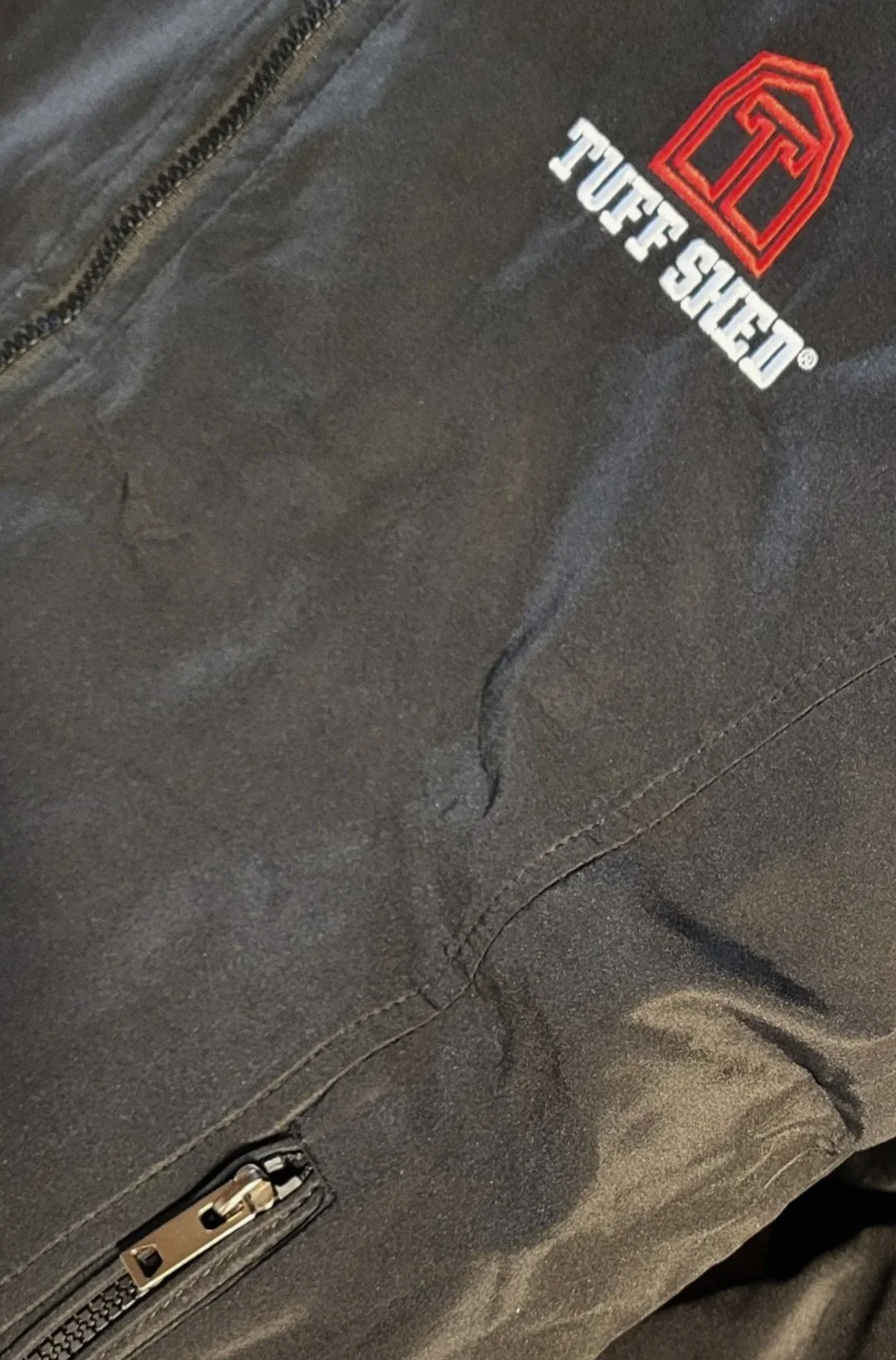 Close-up of a black outdoor jacket with a recognizable red and white 'FUFF SHIELD' logo embroidered on the chest area.