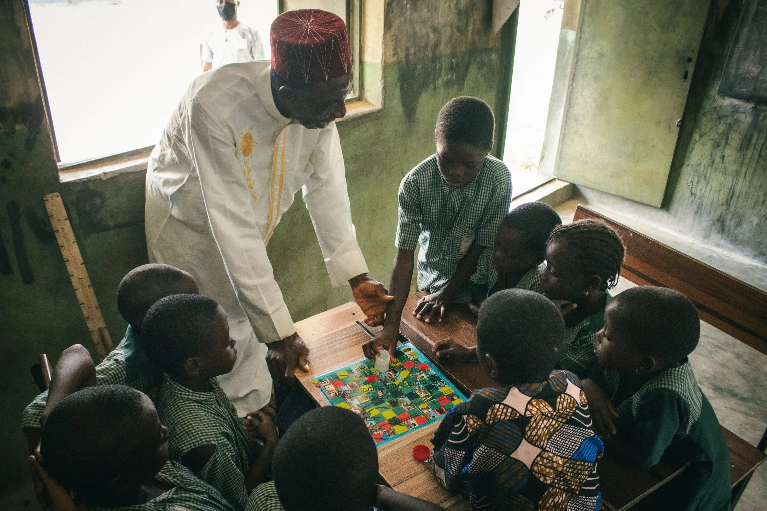 A local Apojola teacher helps students play "Schisto and Ladders", a board game designed by Cynthia Umunnakwe for youth education and awareness surrounding schistosomiasis 