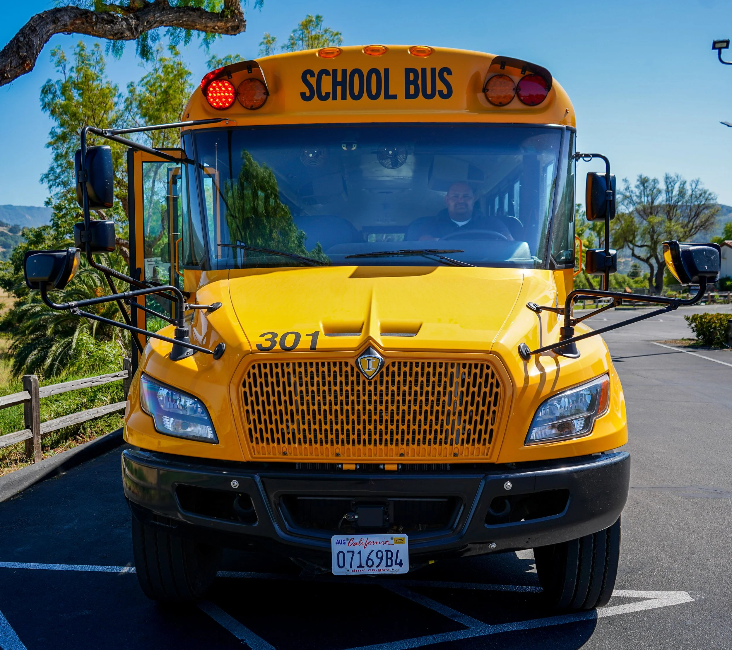Front view of a yellow school bus with a driver inside, parked in a parking lot on a clear day.