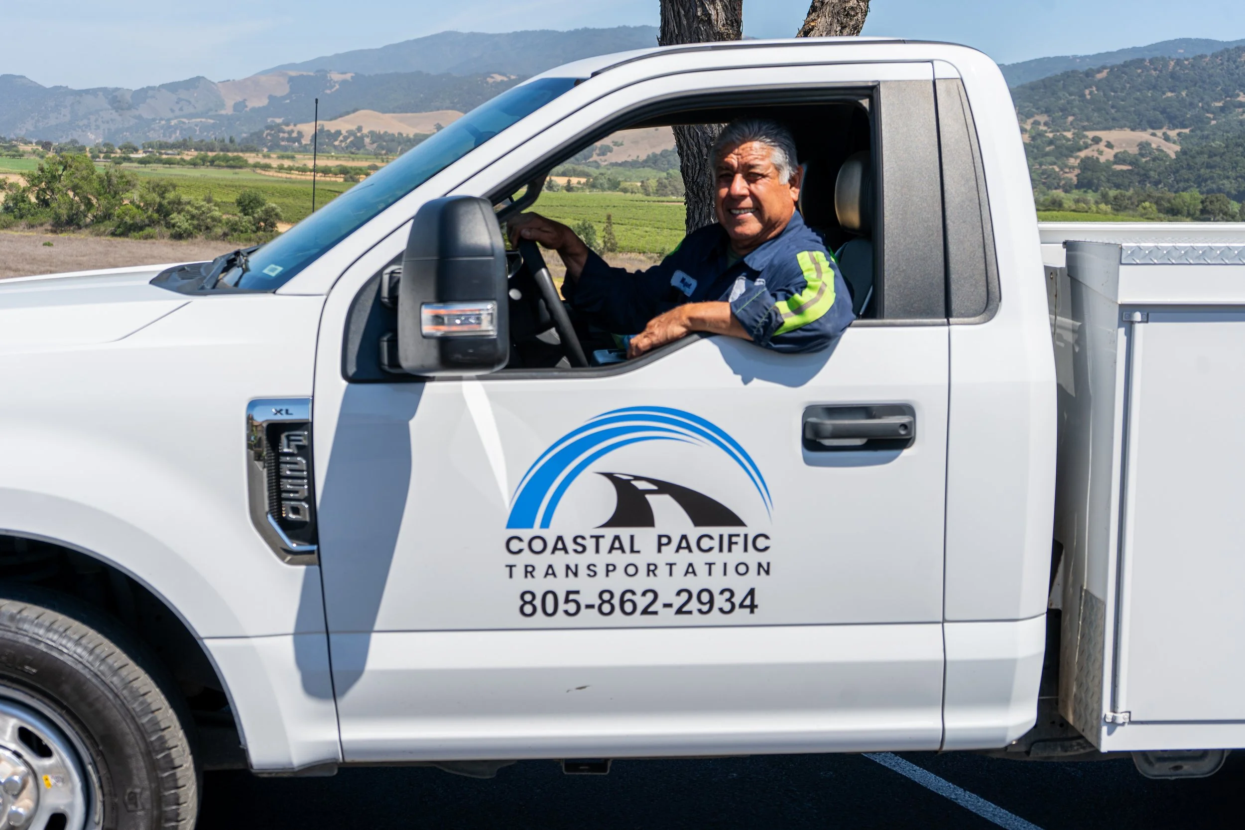 Portrait of a smiling young man with glasses and dark hair, wearing a black shirt, against a plain light background.