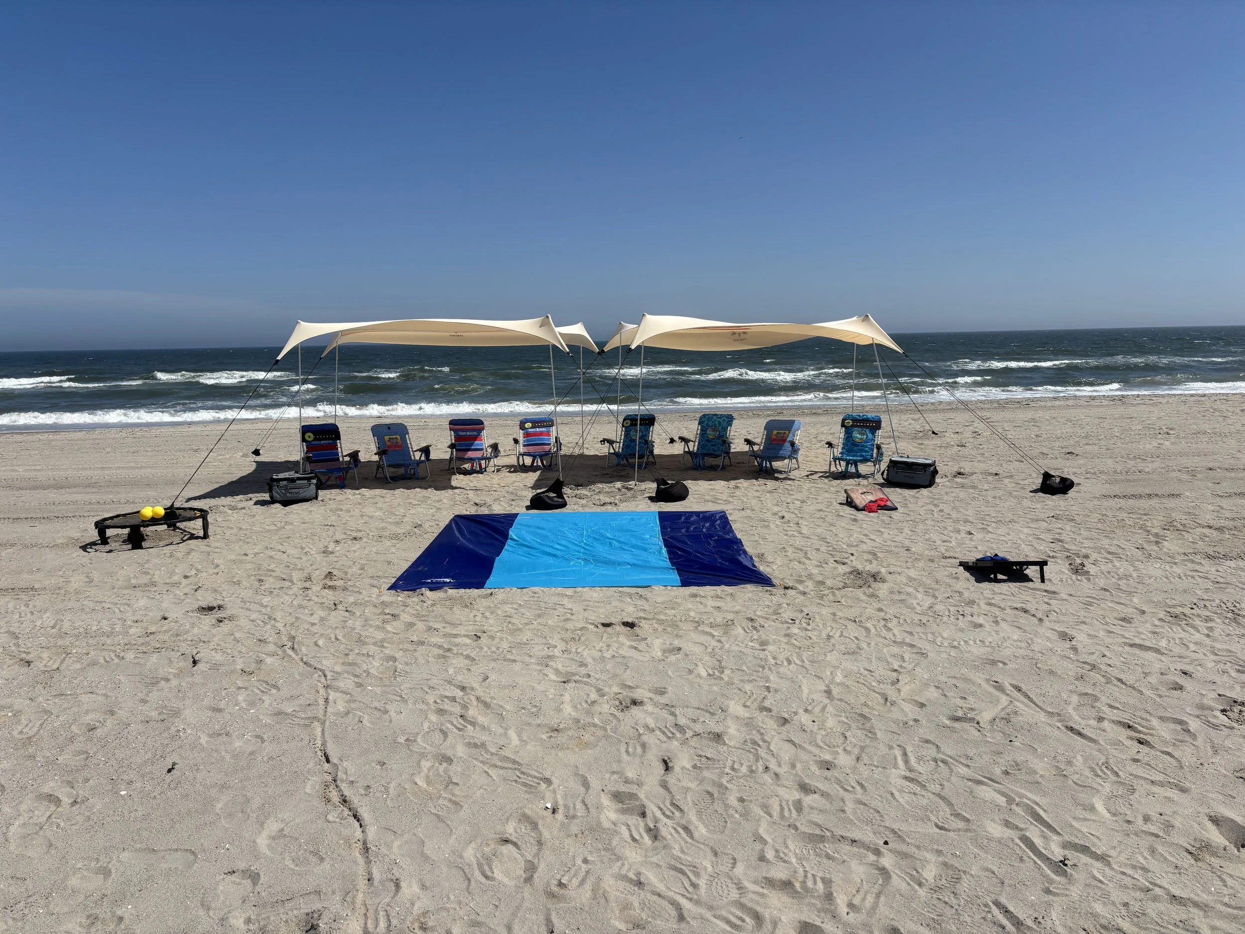 Empty beach chairs and umbrellas set up on sandy beach with ocean waves in the background, under a clear blue sky.