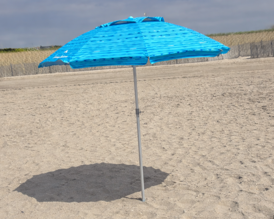 A closed blue beach umbrella with sand and a volleyball net visible in the background.