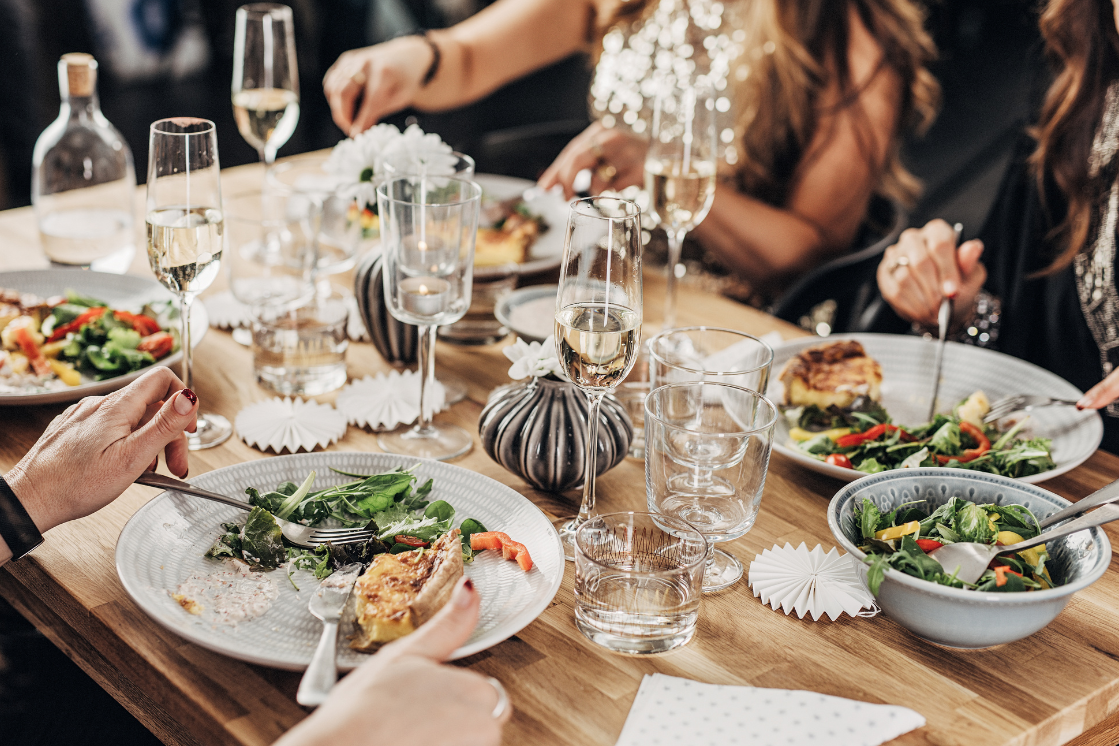 People enjoying a dinner with plates of salad, wine glasses, and a wooden table decorated with candles and flowers.