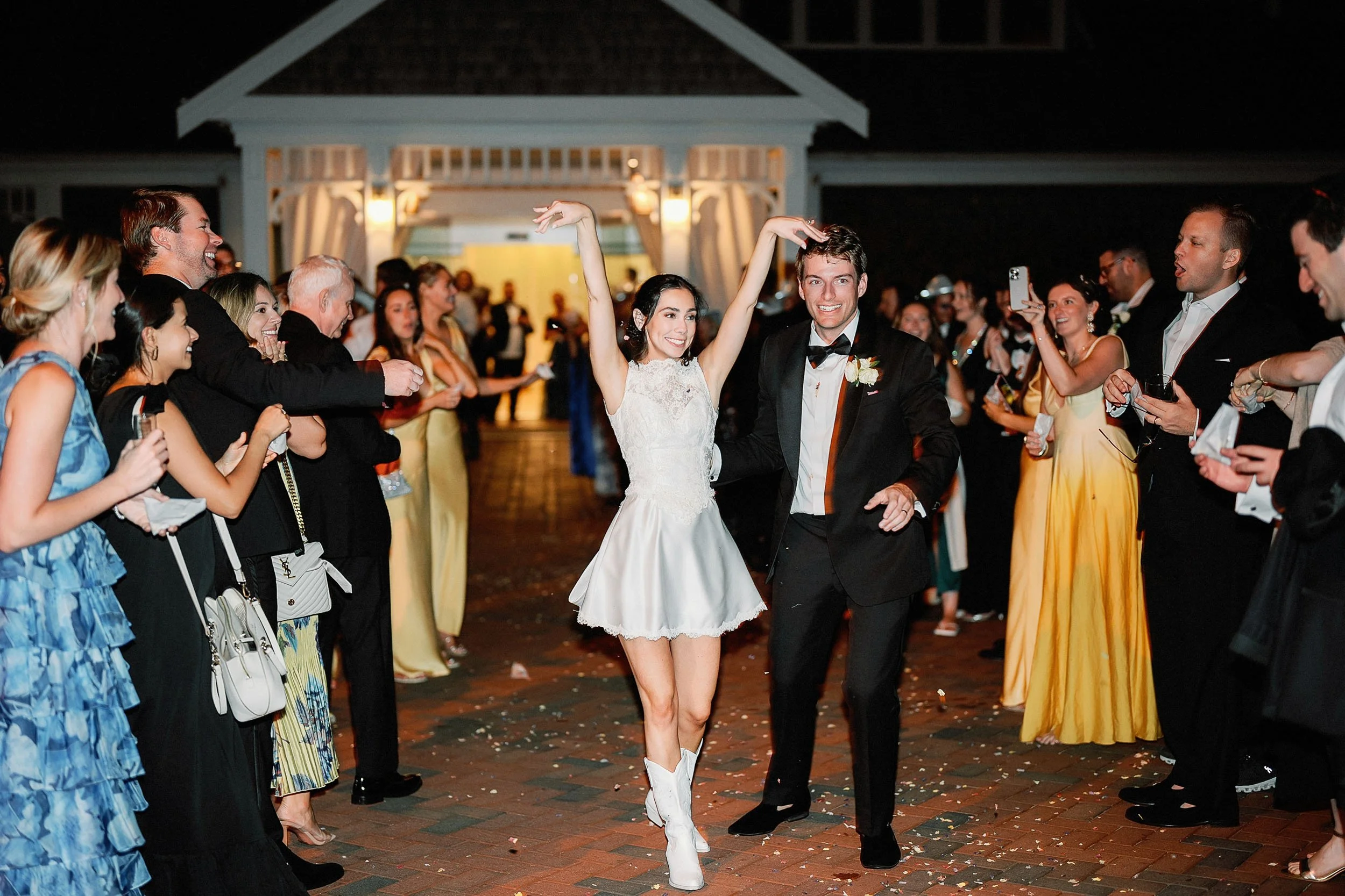Bride and groom dancing at their wedding reception, surrounded by friends and family in formal attire, with joyful expressions and celebratory atmosphere at night.