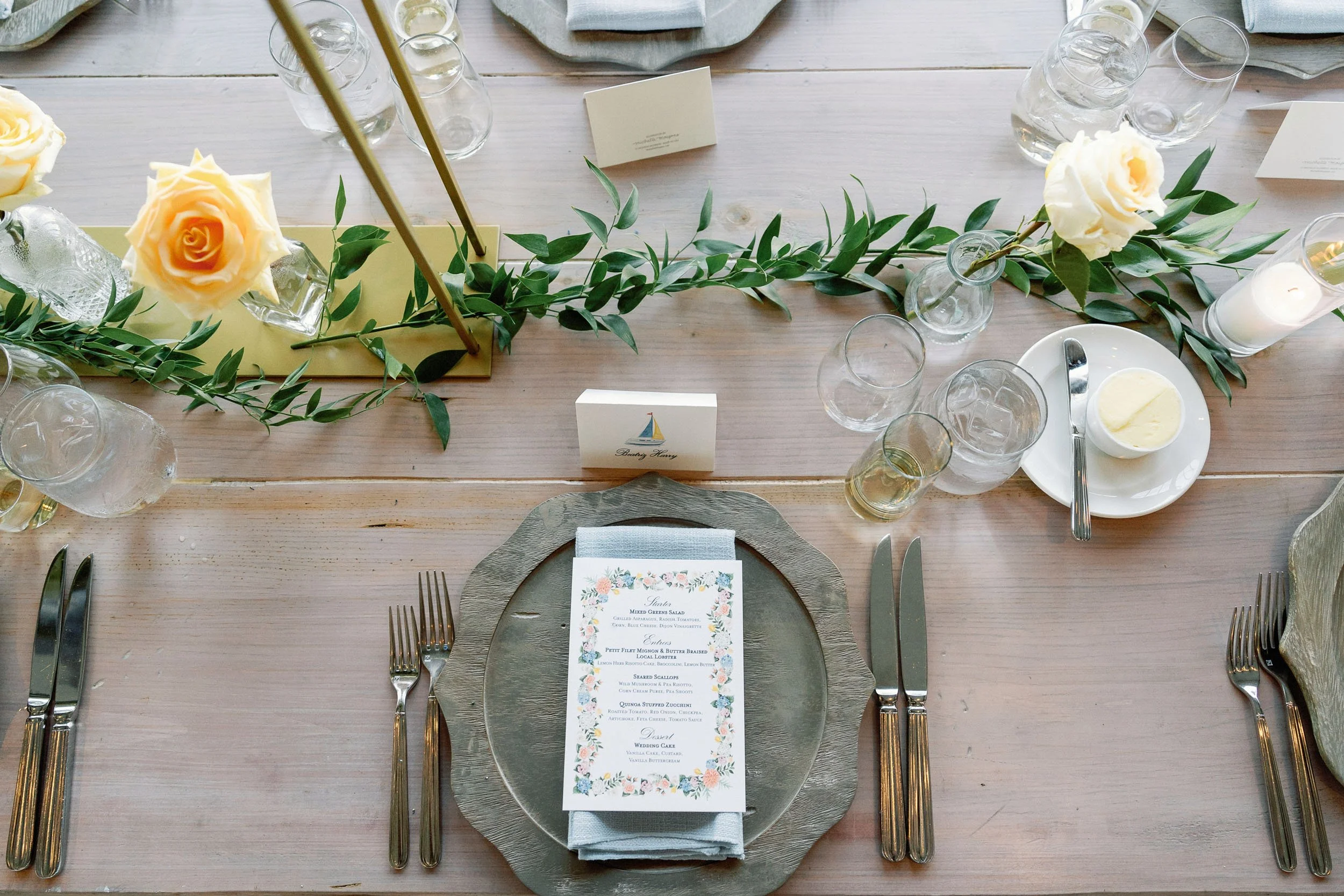 Elegant wedding table setting with a floral centerpiece, glassware, silverware, a menu card, and candles on a wooden table.