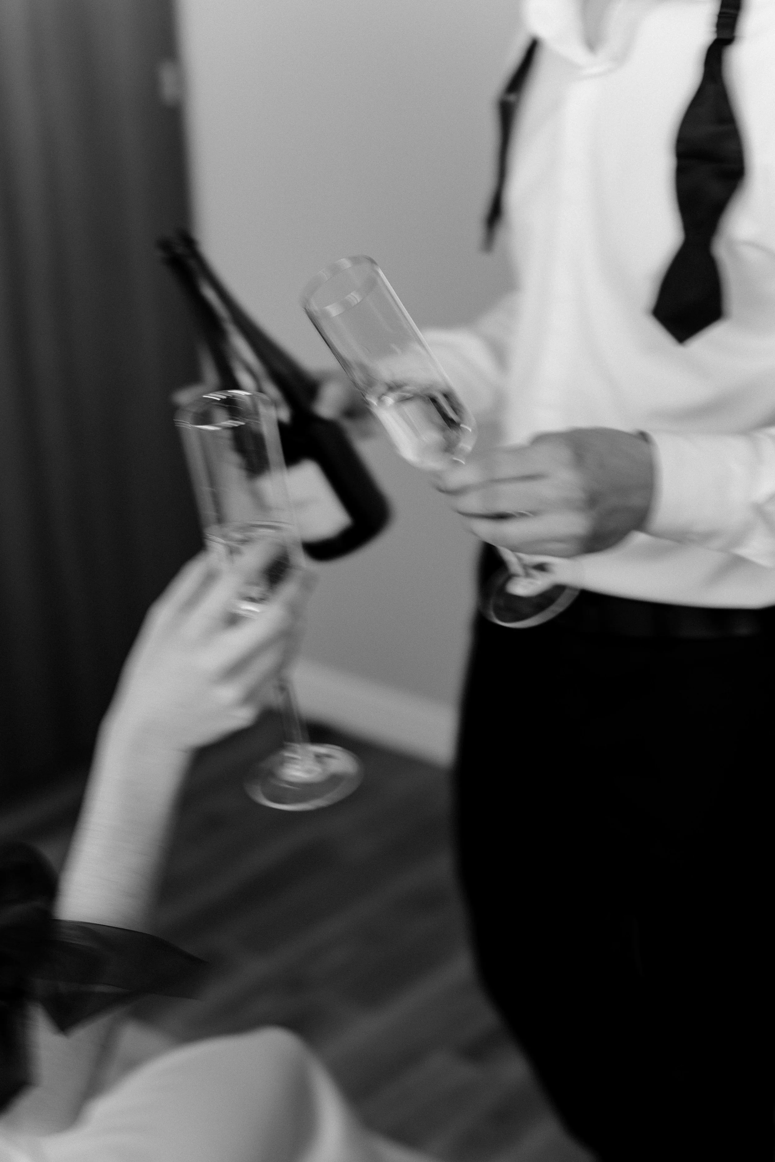People clinking glasses at a celebration or gathering, two holding champagne flutes, one person in a white shirt with a black tie.
