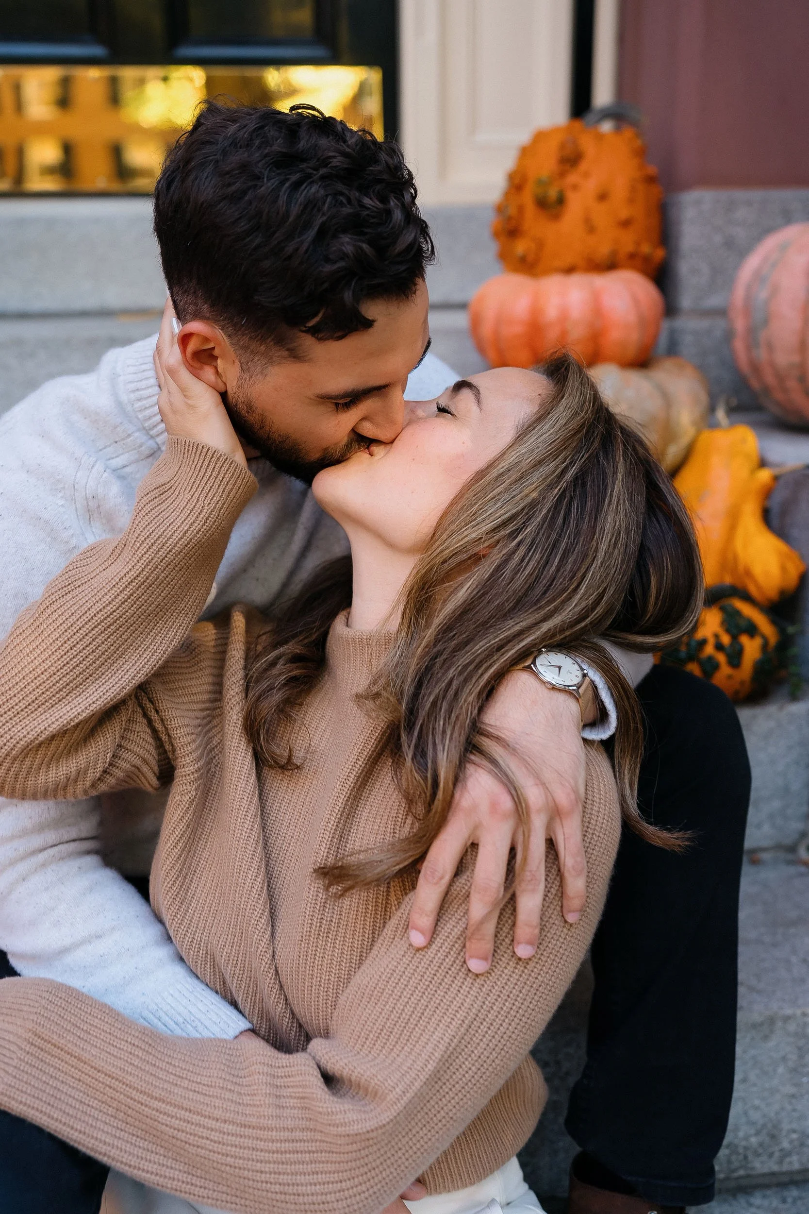A couple sharing a kiss on a porch decorated with pumpkins.