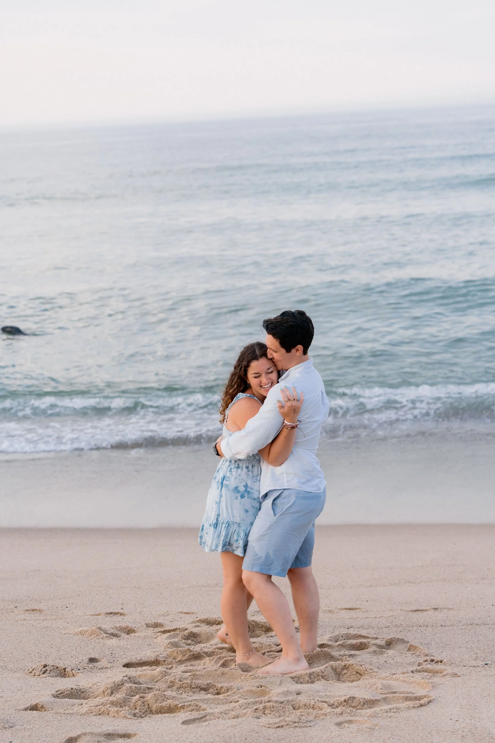 A happy couple hugging on the beach near the ocean with waves in the background.