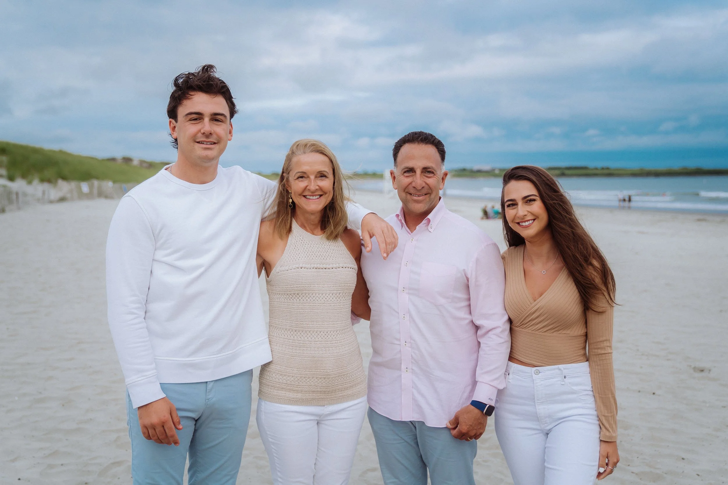 Four people standing together on a beach with a cloudy sky, smiling at the camera.