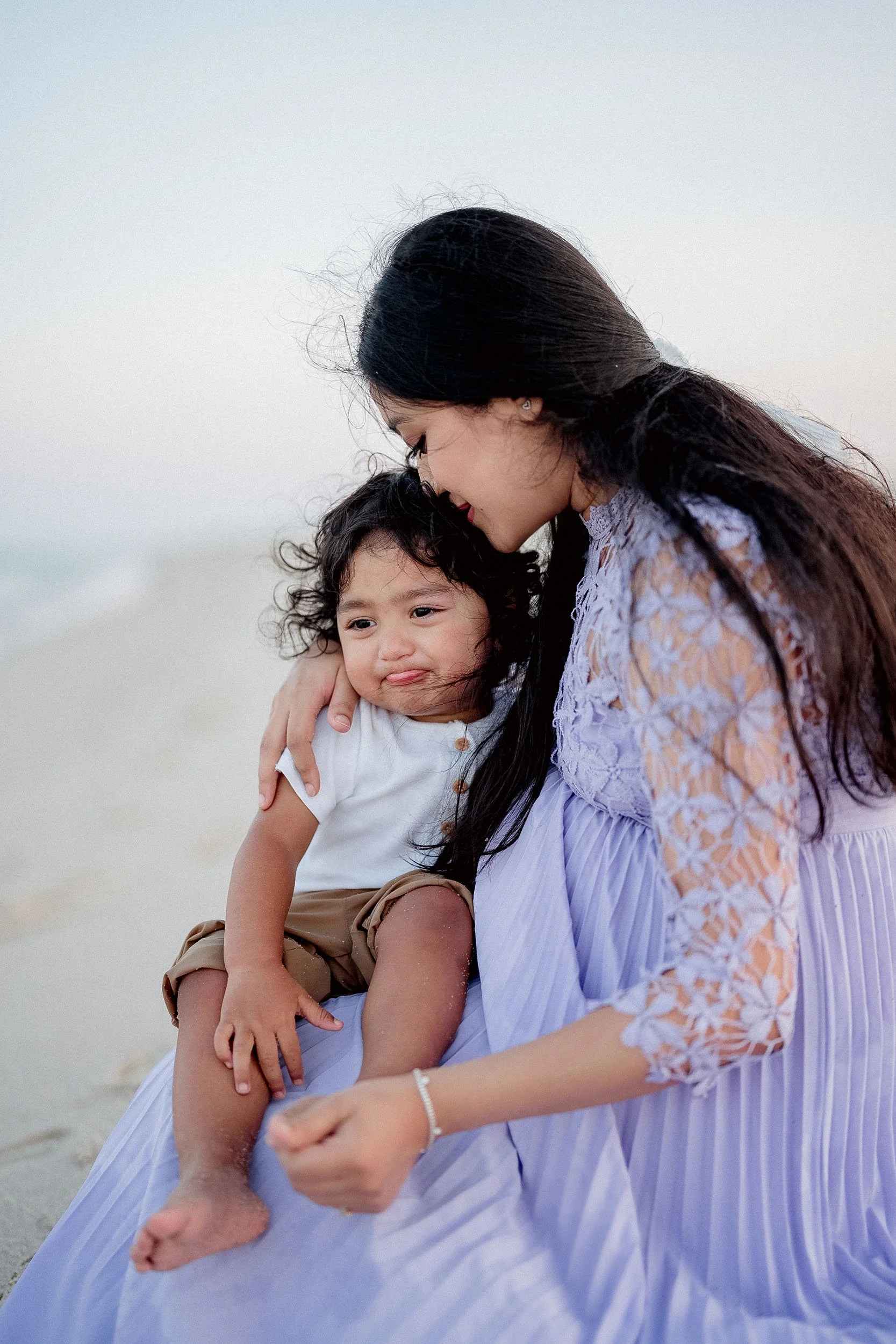 A woman and a young boy at the beach, with the woman embracing the boy who has a sad expression.