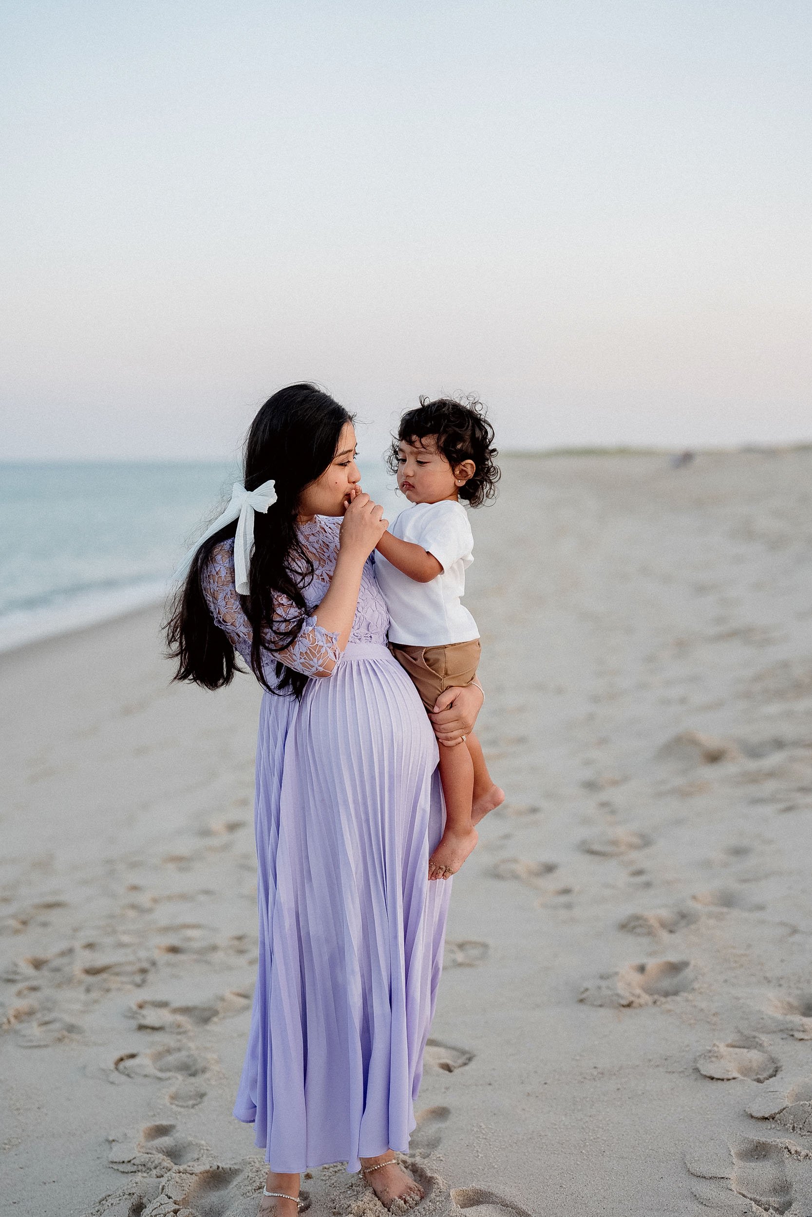 A woman holding a young child on a sandy beach during sunset.