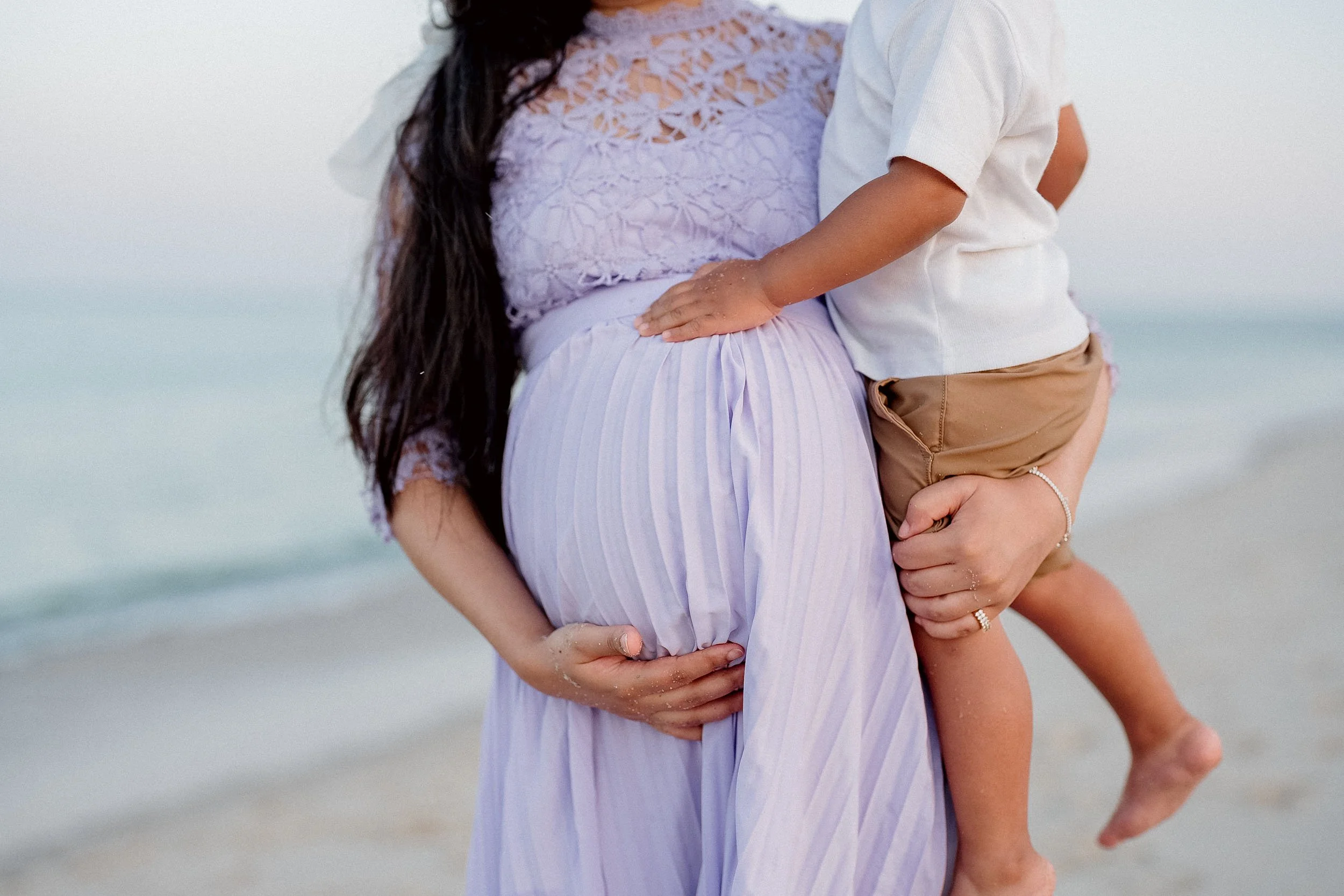 A woman holding a young boy at the beach, with sand on their hands and legs.