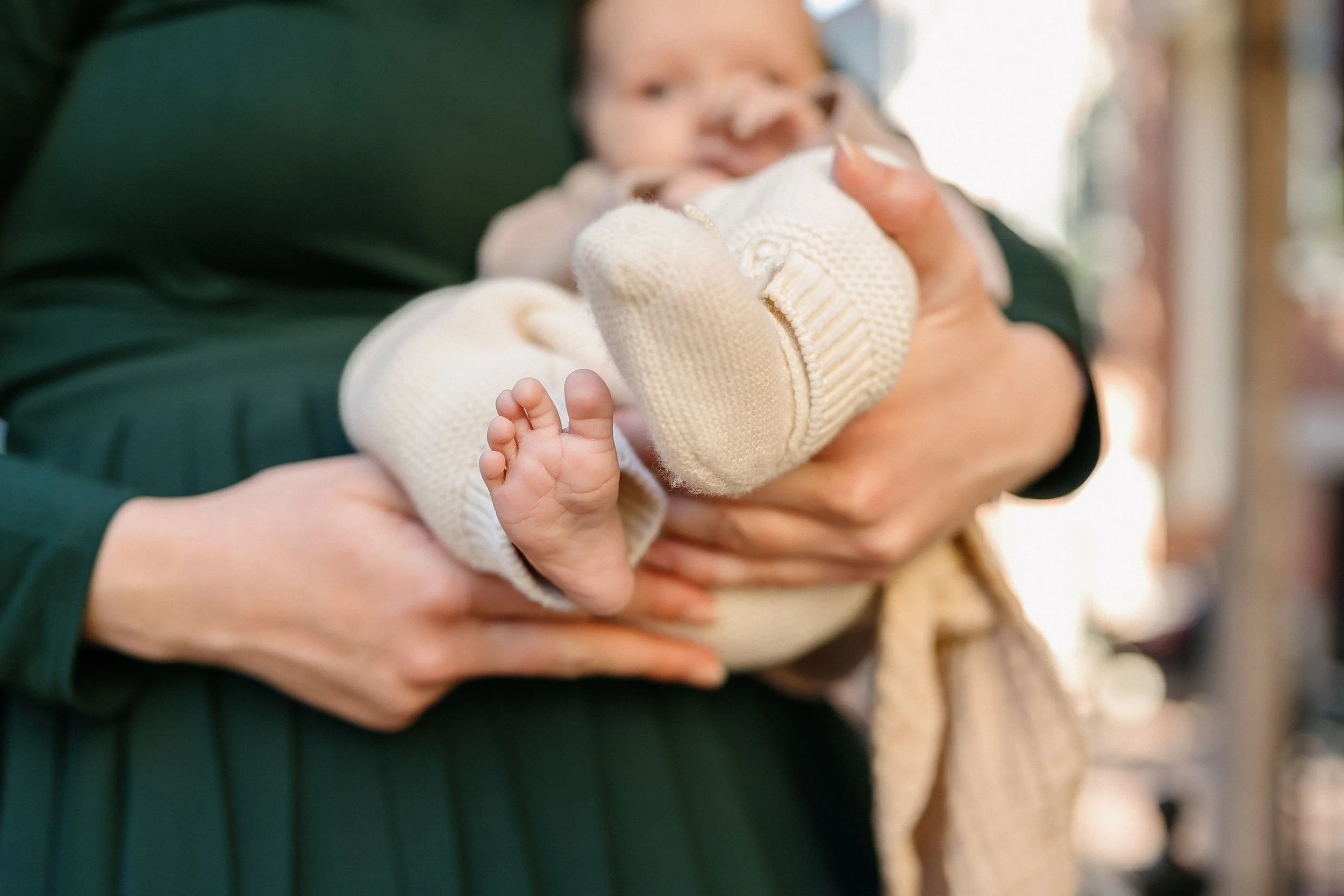 A person holding a baby in their arms, with the baby's tiny foot sticking out from cream-colored knit clothing.