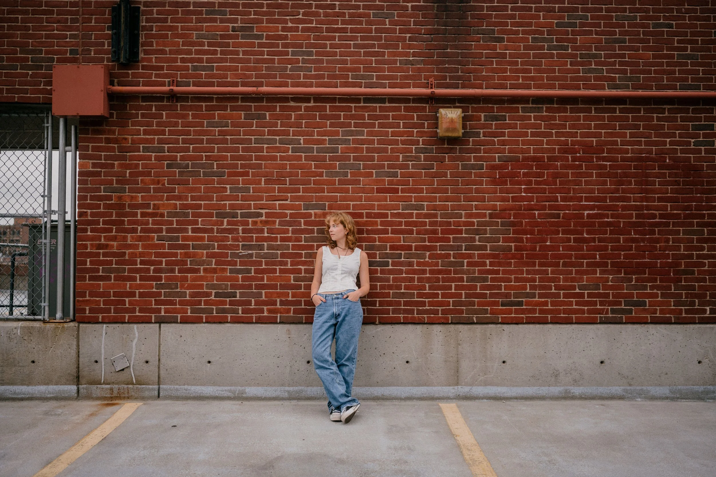 Young woman standing in an empty parking lot against a red brick wall