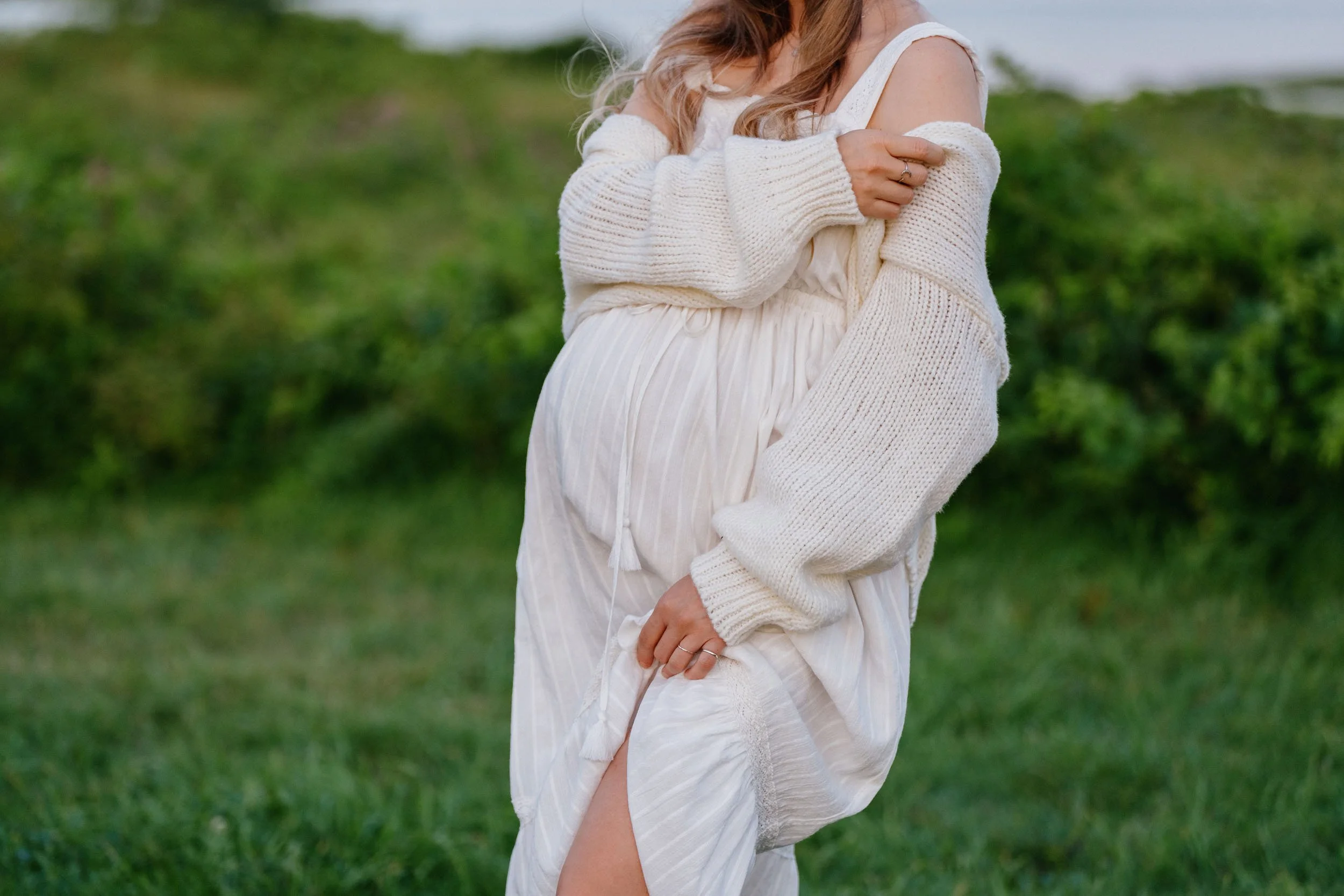 A woman in a white dress and cardigan standing outdoors in a grassy area