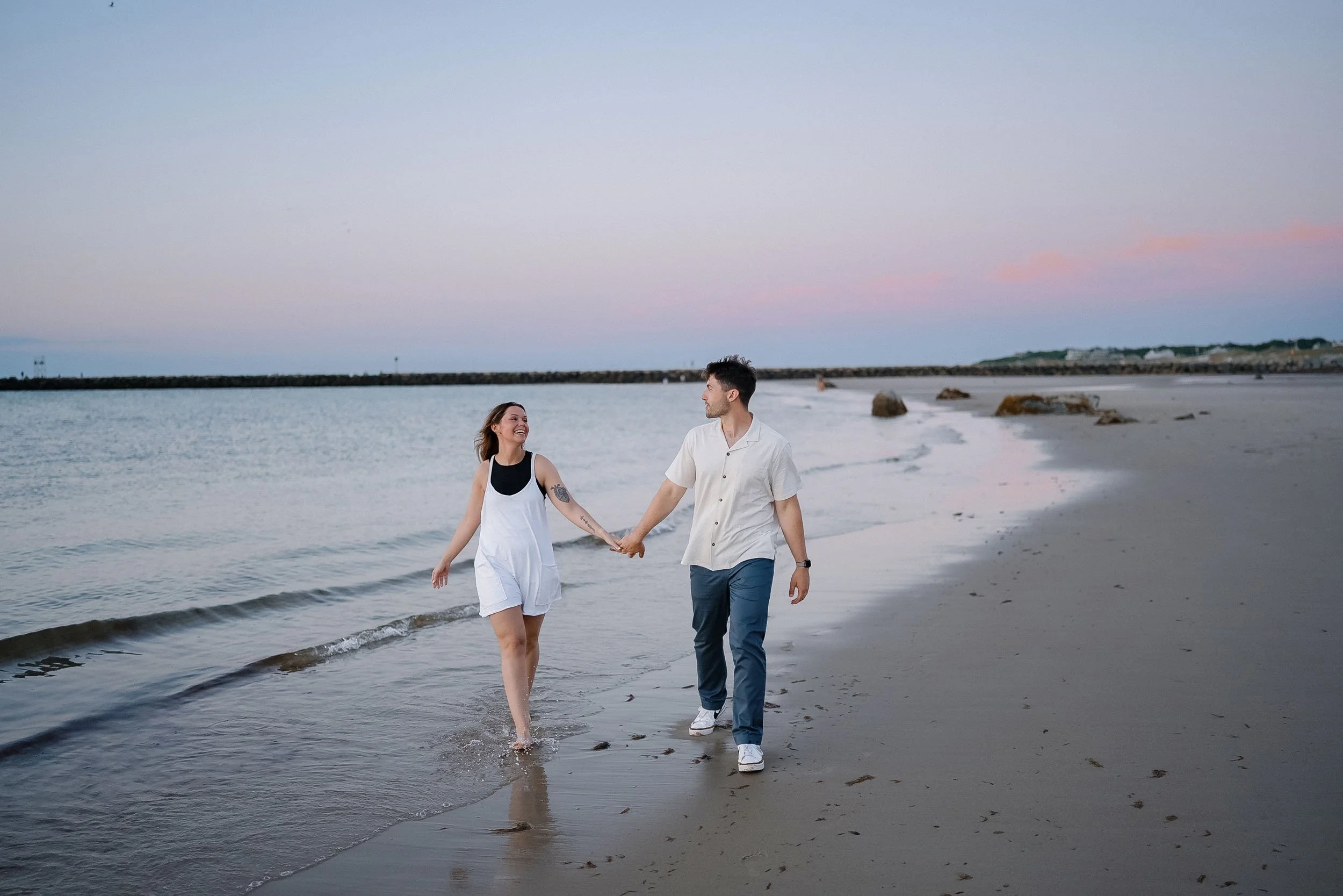 A happy couple walking hand in hand along the beach at sunset.